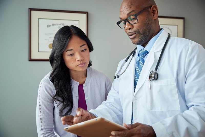 Médico em consulta com paciente, indicando resultado de exames no tablet, para representar o exame admissional