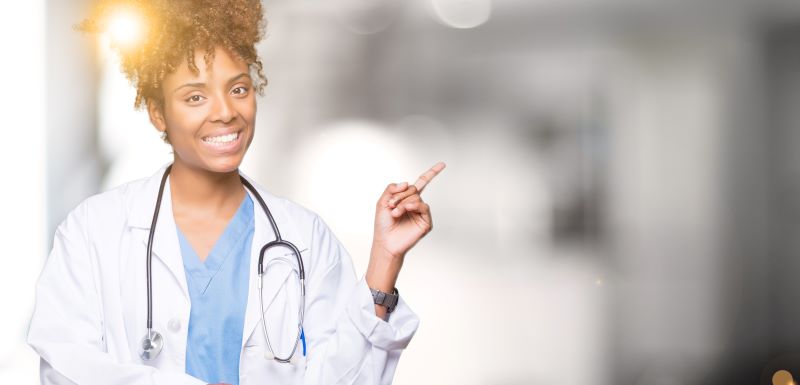 O ASO é emitido por um médico(a) especialista em SST (Saúde e Segurança do Trabalho). Imagem de uma médica sorridente enquanto trabalha.