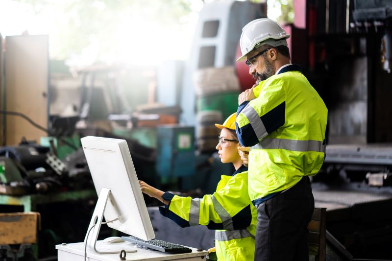 Tecnologia e segurança do trabalho: engenheiros usando EPIs analisando software no computador.