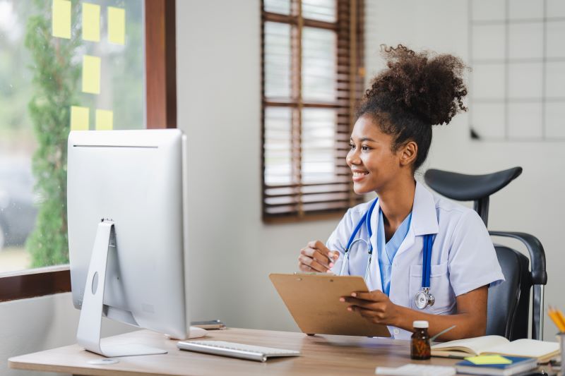 o que é saúde ocupacional​: enfermeira sorridente verificando informações em computador e prancheta